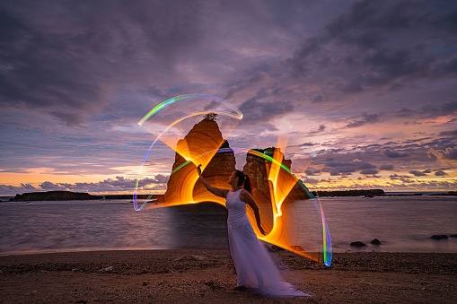 A female light painting model on sandy Tanjung Layar Beach during colorful cloudy sunrise