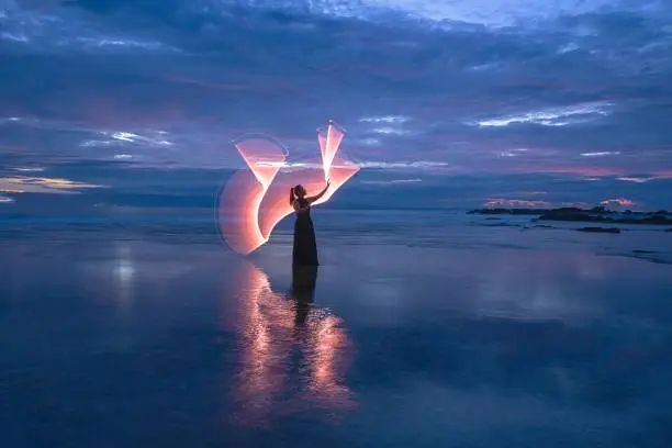 Photo of Female light painting model on sandy Tanjung Layar Beach during beautiful dark blue sunrise