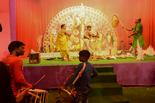 Howrah,India -October 13, 2021 : Dhaakis playing dhaaks while Hindu Priests worshipping Goddess Durga with panchapradip, chamor and hand fan. Ashtami puja aarati - sacred Durga Puja ritual.
