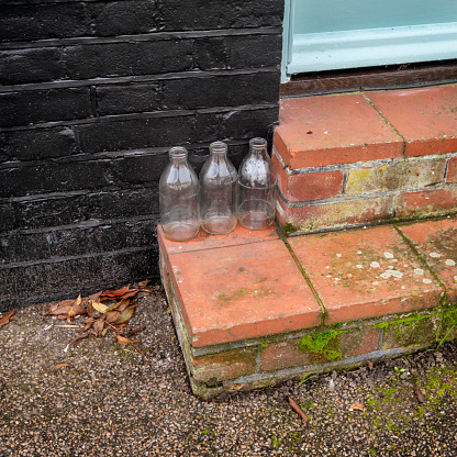 Three empty milk bottles in a row on a doorstep, waiting for the milkman to exchange them for full bottles.