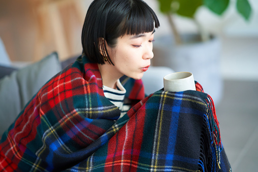 Young woman wearing a blanket and holding a mug