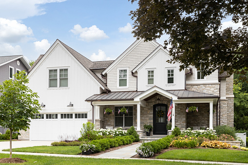 Oak Park, IL, USA - July 8, 2022: A new modern farmhouse with a white and brick siding, covered front porch, and beautiful landscaping.