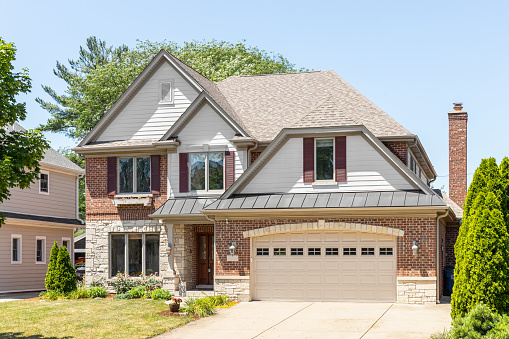 Oak Park, IL, USA - June 4, 2022: A suburban, red brick and white vinyl home with a two car garage, a peak over the front door, and well maintained landscaping.