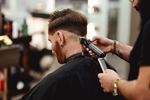 mid adult bearded man visiting hairstylist in barber shop.