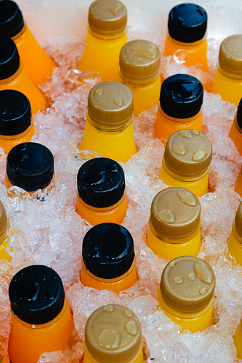 Orange juice or lemonade bottles in a box of ice, close up.