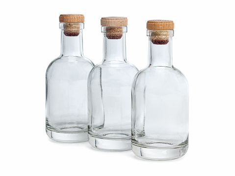 Three empty glass bottles with cork insert in a line on a white background.