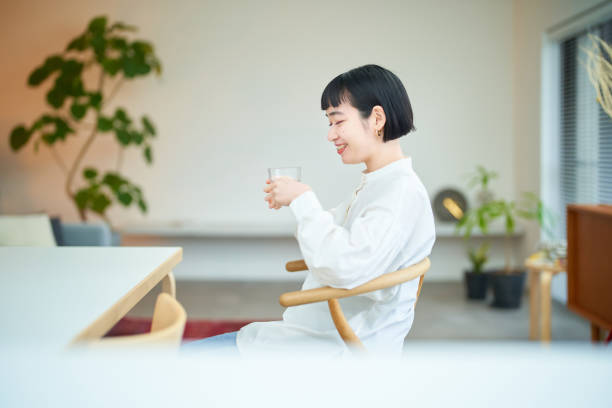 部屋で水を飲む若い女性 - water plant ストックフォトと画像