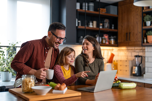 Young family watching tutorials on a laptop and about to prepare a delicious lunch with lots of fresh ingredients.