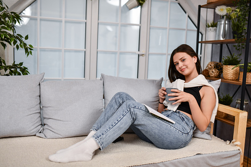 Beautiful Female Holding Cup While Reading Favorite Book At Home And Sipping Coffee