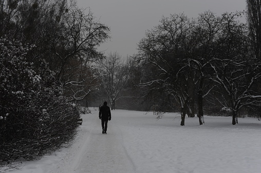 Person walking in the street in a city during snowstorm with snowy path in winter in Europe