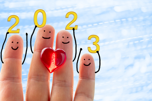 Happy finger family with a red heart holding 2023 numbers. Blue background with defocused lines and spots. Space for copy.