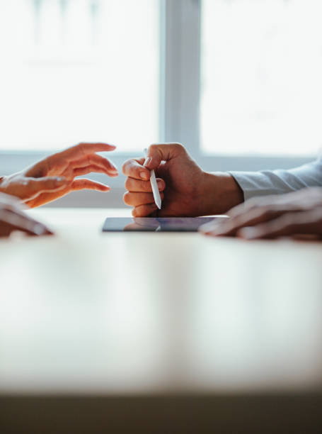 Unrecognizable team of two colleagues talking and reading business report on a tablet while standing at office desk together.