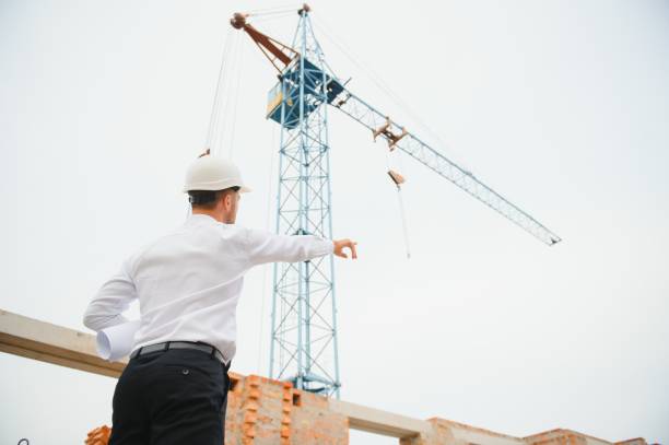 istock Construction engineer supervising progress of construction project stand on new concrete floor top roof and crane background. 1451137443
