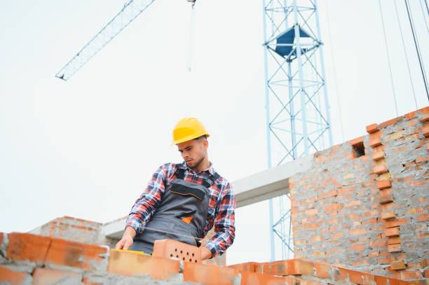 istock Using bricks. Young construction worker in uniform is busy at the unfinished building 1451137867