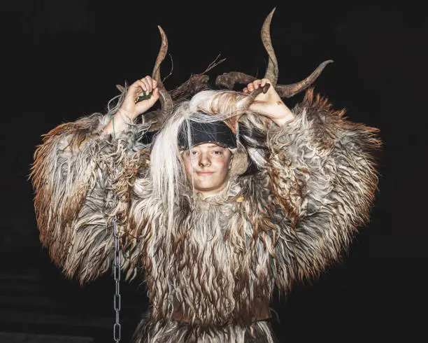 Portrait of a boy in a krampus costume, a heavy sheepskin and a mask with horns, Austria; Salzburg