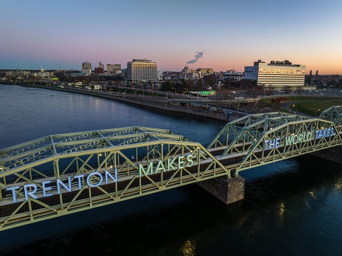 A drone shot of suspension bridge over river at sunrise and Trenton cityscape in the background in New Jersey