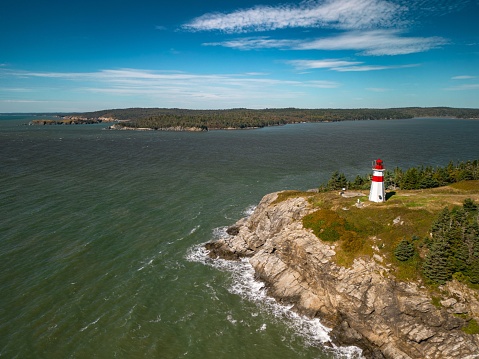 An aerial view of a white-red lighthouse on the edge of a cliff