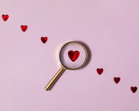 Creative searching for love concept, Red hearts and magnifying glass on light purple background. Minimalistic Valentine's day composition.