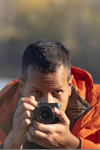 Portrait of traveler man at lake in autumn taking a photo with the digital camera. High quality photo
