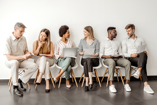 Multicultural diverse candidates sit on chairs wait for interview have fun talking, happy multiethnic diverse applicants speak and chat joke laugh before hiring process, employment concept
