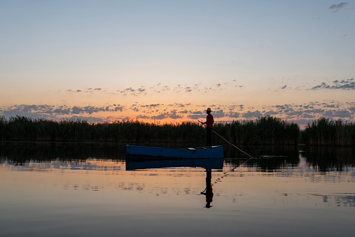 Fisherman in front of an early morning sunrise sky fishing out of his boat during a summer sunrise on lake