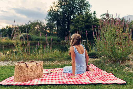 Teenage girl enjoying picnic in nature. The girl is sitting on the blanket, having cookies and reading a book.\nCanon R5