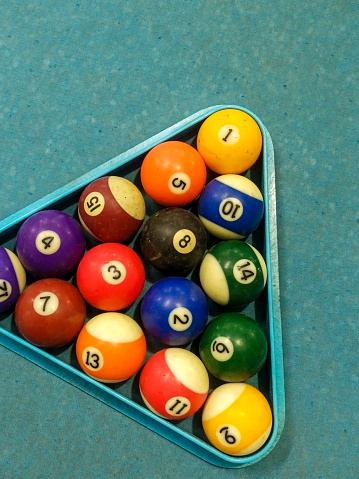 colored balls with numbers for billiards standing in a triangle shape on a blue table before the first serve of the ball. Game concept for weekend