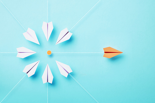 Paper planes are flying towards an orange point whilst an orange plane is flying away on blue background, Target concept.