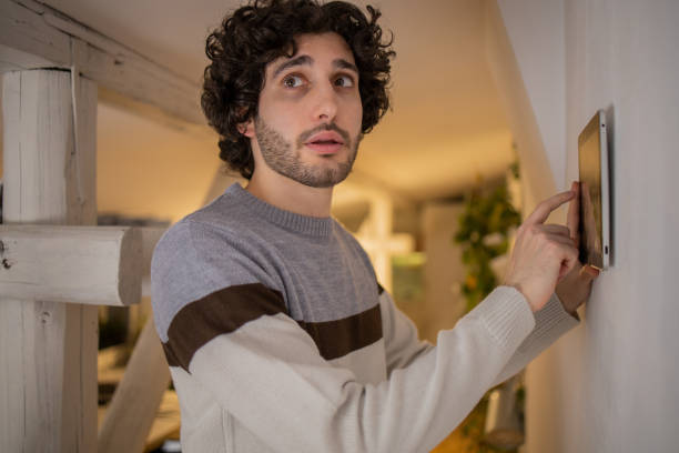 istock Young man adjusts the temperature at home with a device on the wall 1451181137