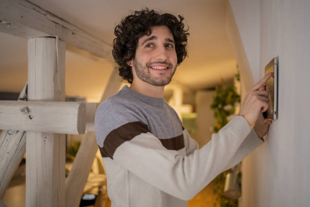 istock Young man adjusts the temperature at home with a device on the wall 1451181187