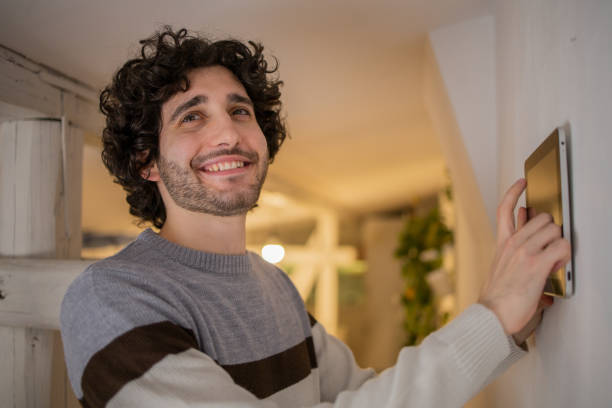 istock Young man adjusts the temperature at home with a device on the wall 1451181293
