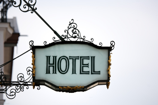 old-fashioned metal hotel sign with ornament against overcast sky, low angle view