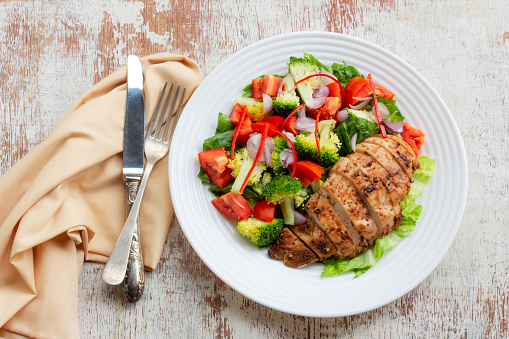 Grilled chicken vegetable salad in plate on white wood background top view, healthy food concept.