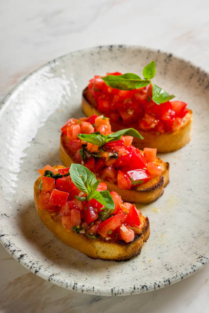 bruschetta com cubos de tomate fatiados e manjericão no prato na mesa de mármore vertical - bruschetta - fotografias e filmes do acervo