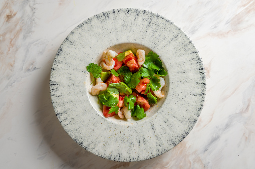 salad with shrimp, avocado and tomatoes on a plate on marble table top view