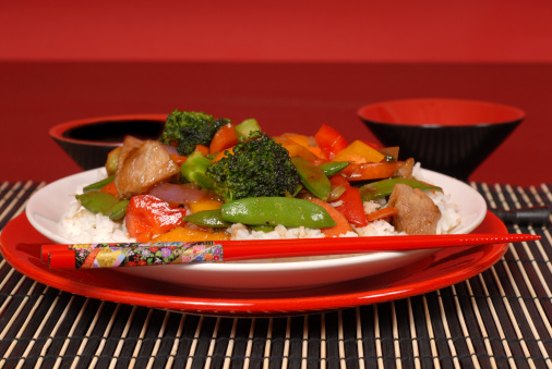 Plate of stir fry pork with chop sticks with red background