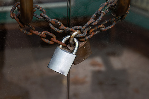 Silver padlock and rusty chain securing a double glass door.