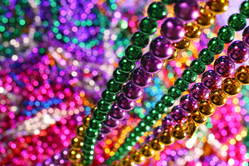 Mardi Gras theme colored beads hang in focus as a pile of beads fills the background
