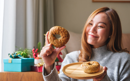 Portrait image of a young woman in sweater holding a plate of bagel with Christmas holiday decoration at home