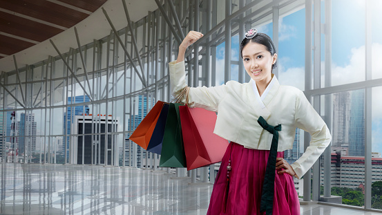 Asian woman wearing a traditional Korean national costume, Hanbok, standing while holding a shopping bag in the mall