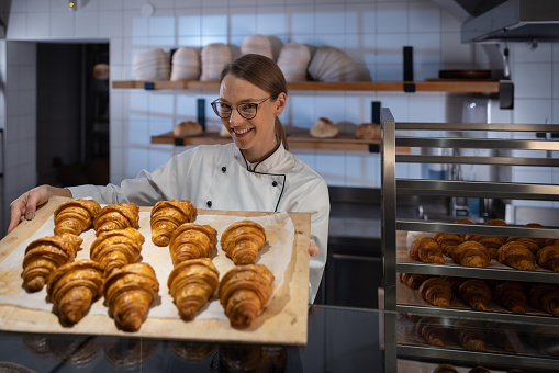 Closeup fresh baked brown bread roll in hands of female baker. Wheat bread on wooden table in bakery. Chef demonstrating the perfectly baked bread. Healthy choice, warm from the oven dusted with flour