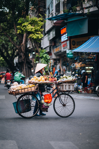 Hanoi, Vietnam - November  21, 2022:Woman pushing her bicycle loaded with fresh fruits at the famous Old Quarter in downtown Hanoi, Vietnam. Everyday Street Life.