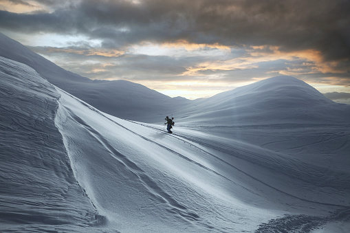 awesome view of the high snow-capped mountain range and skier walking along it. Fog clouds and colorful sky in the background, Caucasus, Georgi