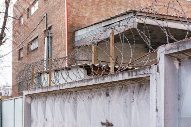 istock Barbed wire above concrete fence of prison. Wall. Security. Control. Danger. Limitation. Forbidden. Prohibition. Prisoner. Sharp. Spiral. Prisoned. Criminal. Crime 1451240842