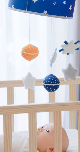 cute newborn baby in crib at home and he is watching toys which hanging above cot