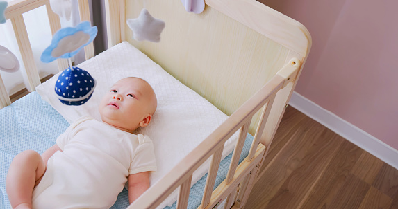 top view of cute newborn baby in crib at home and he is watching toys which hanging above cot