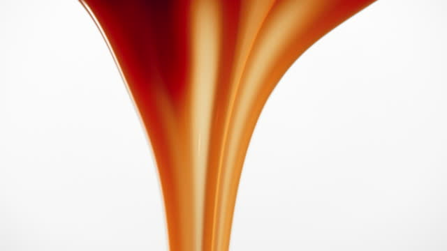 Dripping caramel droplets flowing down liquid sweet sauce on white background