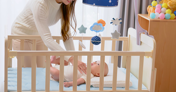 asian mother is comforting cute newborn baby to sleep while infant lying on crib at home