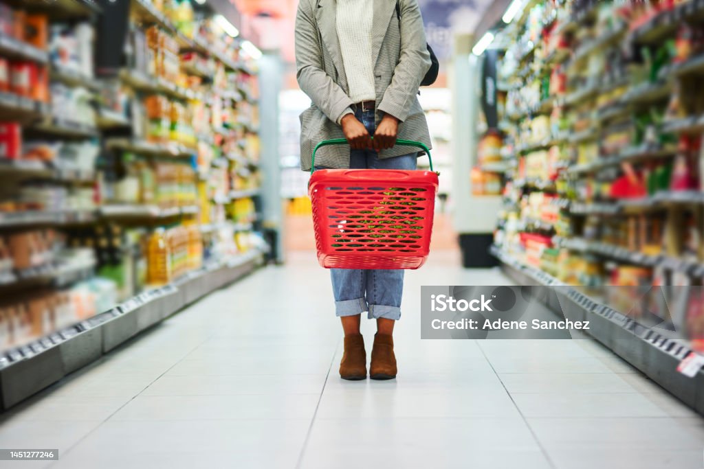 Supermarket aisle, woman legs and basket for shopping in grocery store. Customer, organic grocery shopping and healthy food on groceries sale shelf or eco friendly retail purchase in health shop Supermarket Stock Photo