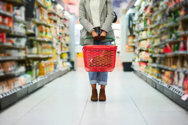 Supermarket aisle, woman legs and basket for shopping in grocery store. Customer, organic grocery shopping and healthy food on groceries sale shelf or eco friendly retail purchase in health shop